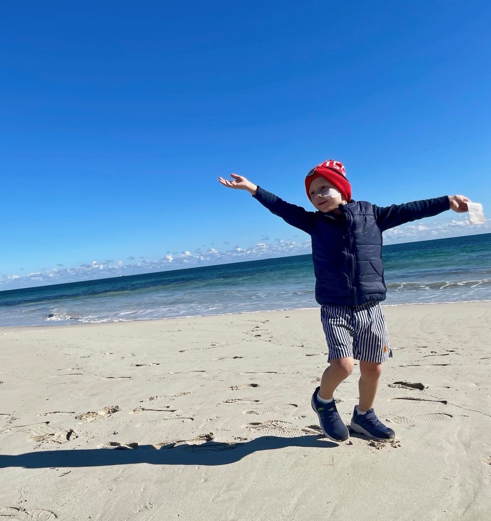 Ruben standing joyfully on the beach beneath the blue sky